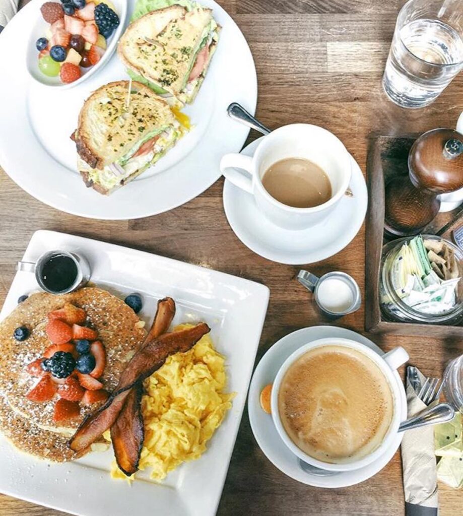 Birds-eye view of breakfast at Cafe Vida, including pancakes, bacon, fruit, syrup, breakfast sandwiches and coffee